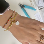 Hand wearing gold bracelet with clover charm, surrounded by jewelry-making tools on a white surface