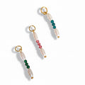 Three pearl charms with a central colored bead, in green, blue, and pink, attached to gold-colored rings.