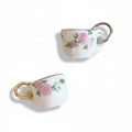 Two small ceramic teacup charms with floral designs on a white background