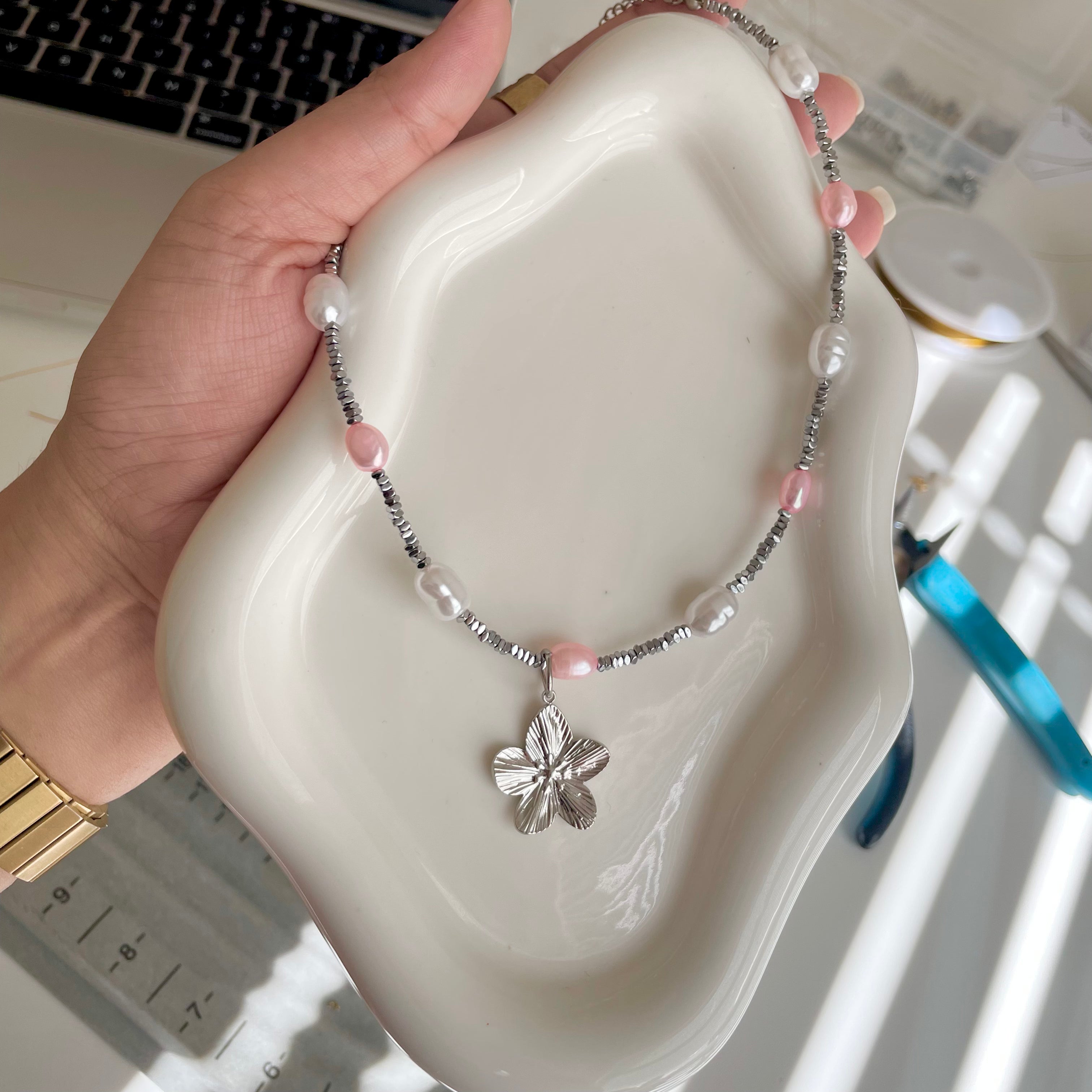Necklace with a floral pendant held over a white dish on a desk.