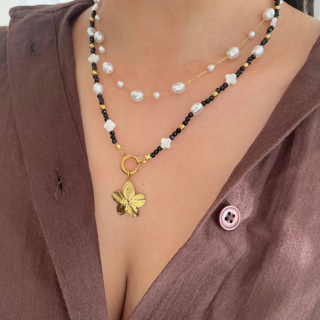 charm necklace with a flower charm pendant worn by a person in a brown top