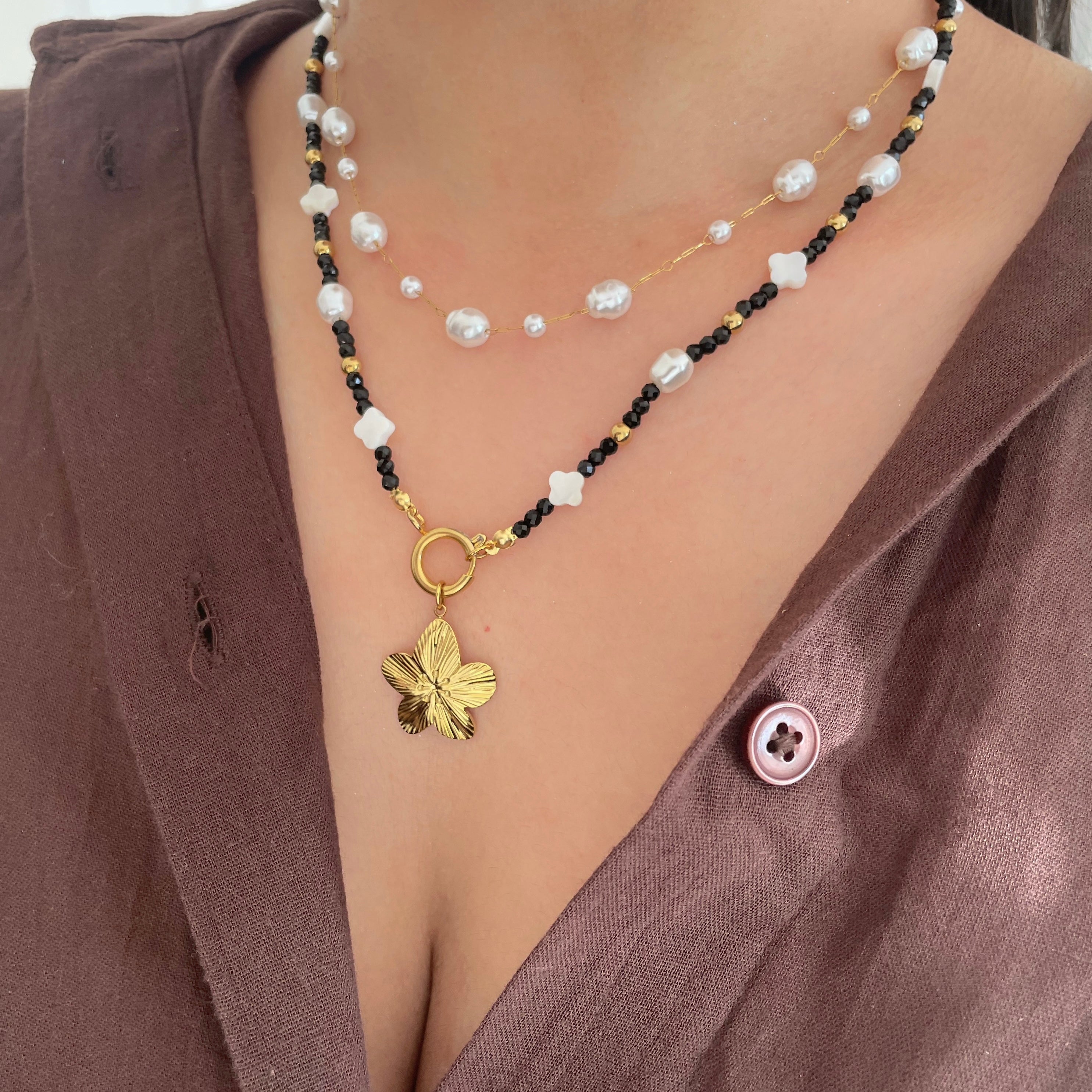 charm necklace with a flower charm pendant worn by a person in a brown top
