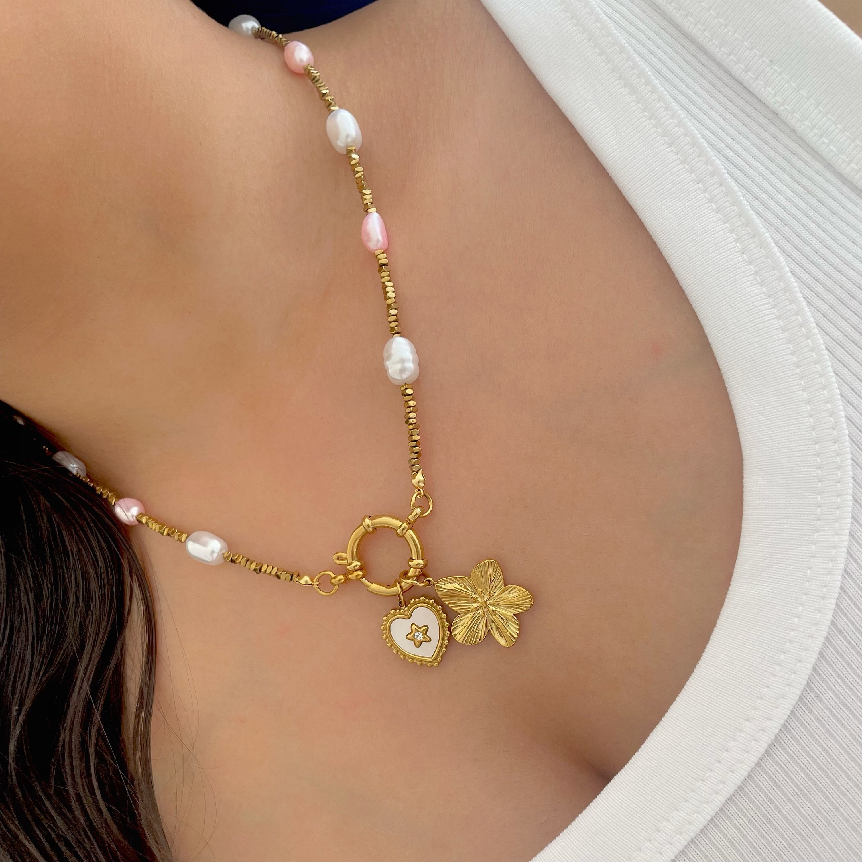 Necklace with gold chain and heart-shaped pendant on a person wearing a white top.