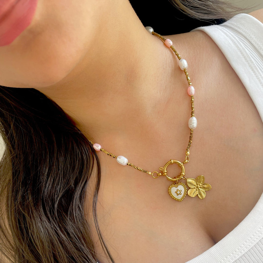 Necklace with gold heart and flower charm worn by a person