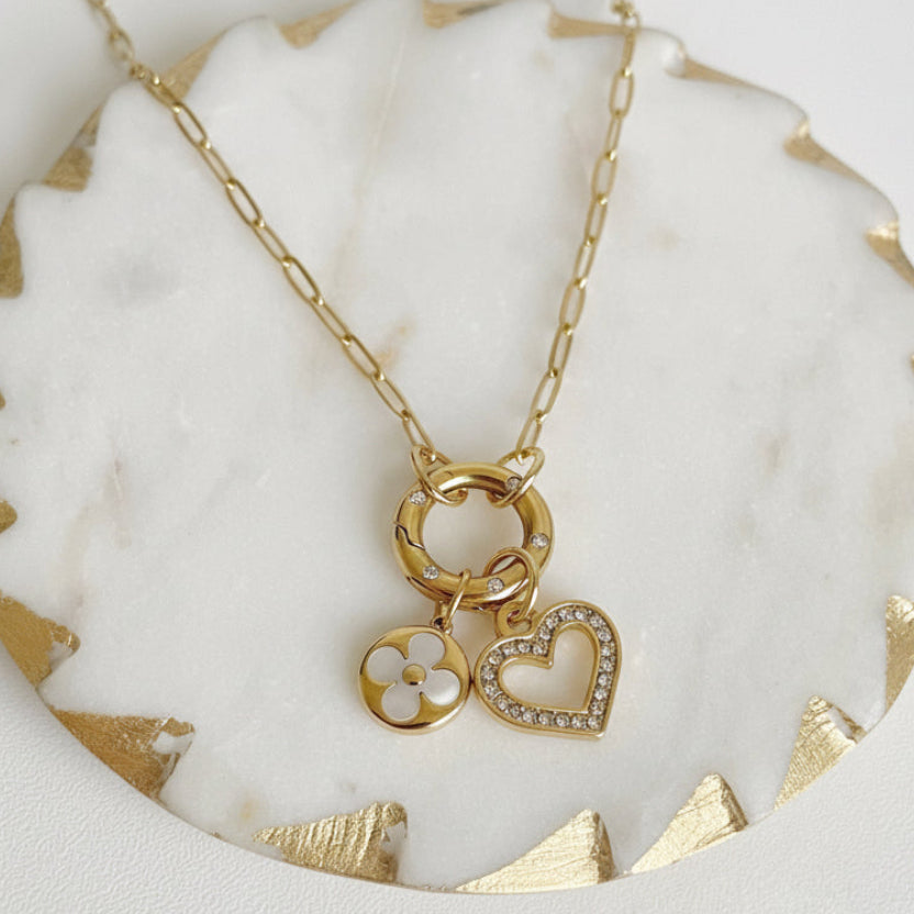 Gold necklace with heart and clover charms on a marble surface