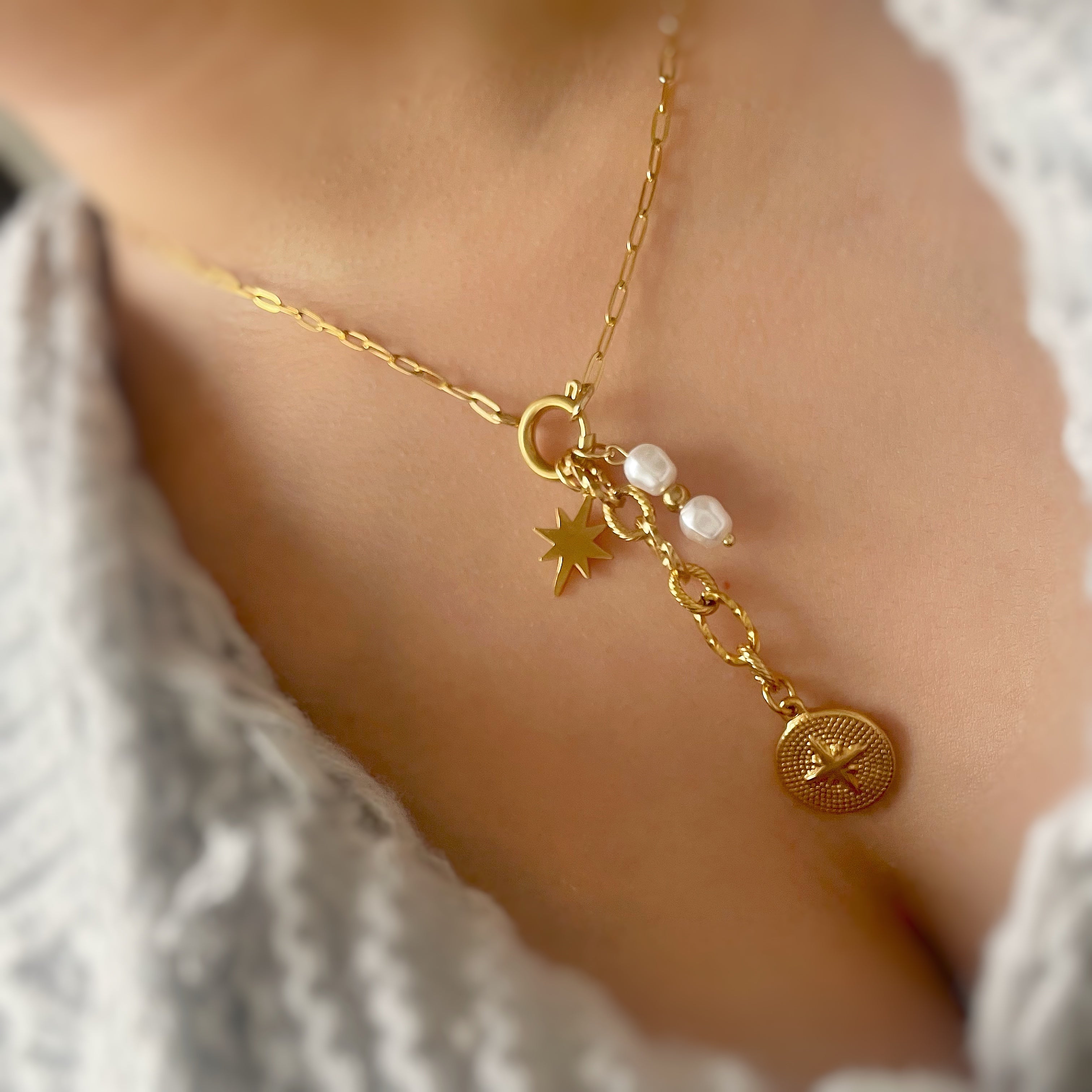 Gold necklace with charms on a person's neck against a neutral background