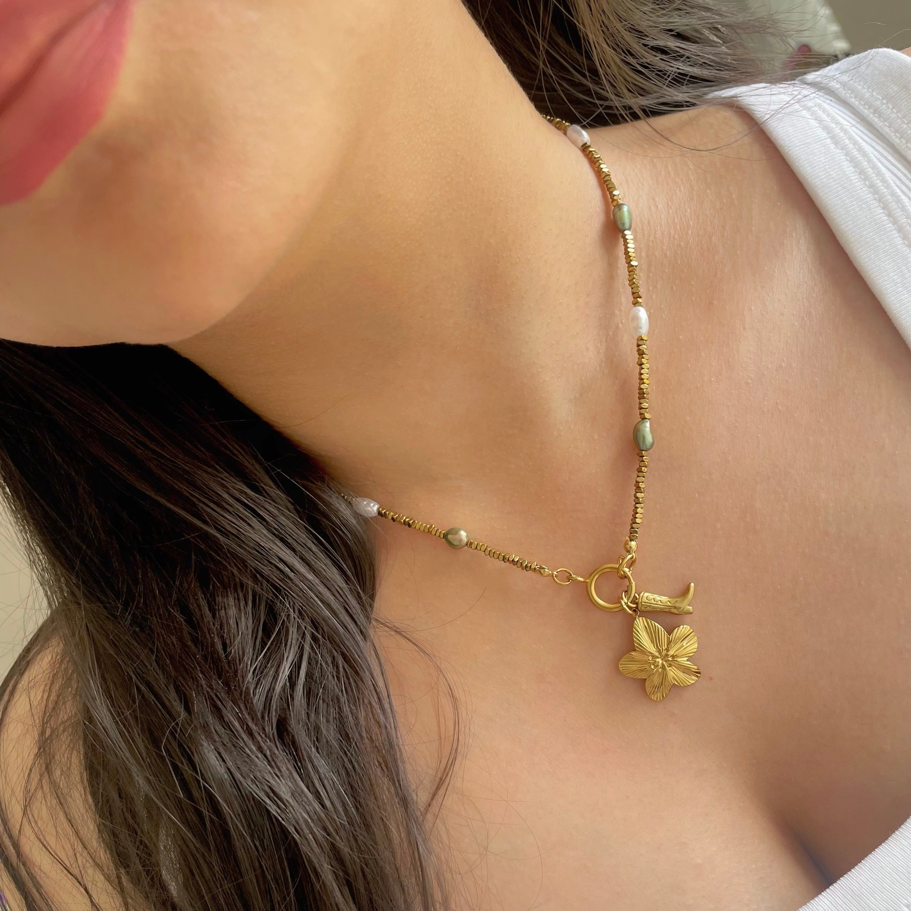 Gold necklace with acowboy boot charm and flower charm  pendant on a person wearing a white top.
