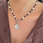 Necklace with a flower pendant worn by a person in a brown shirt.