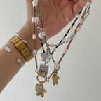 Hand holding multiple beaded necklaces with various charms on a plain background