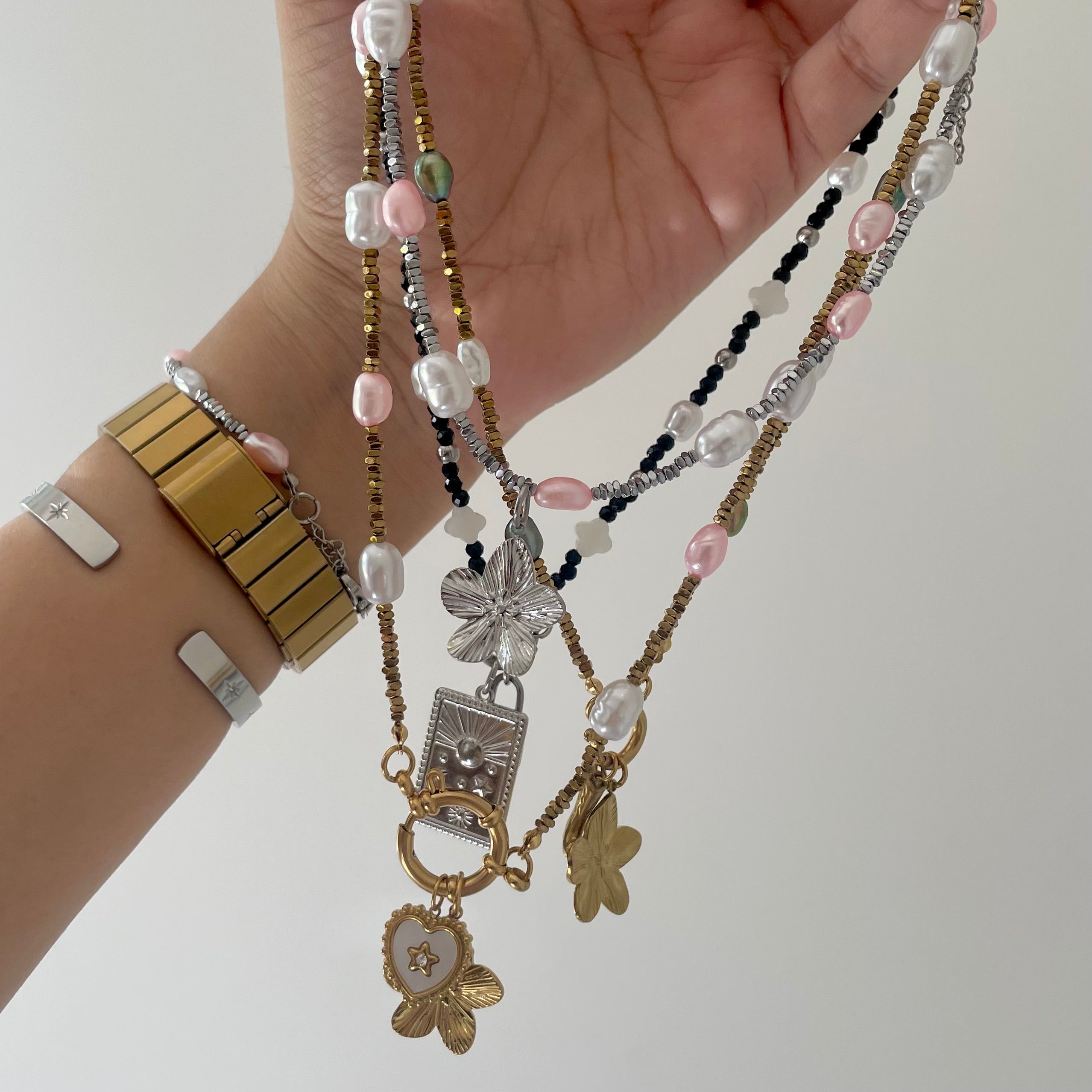 Hand holding multiple beaded necklaces with various charms on a plain background
